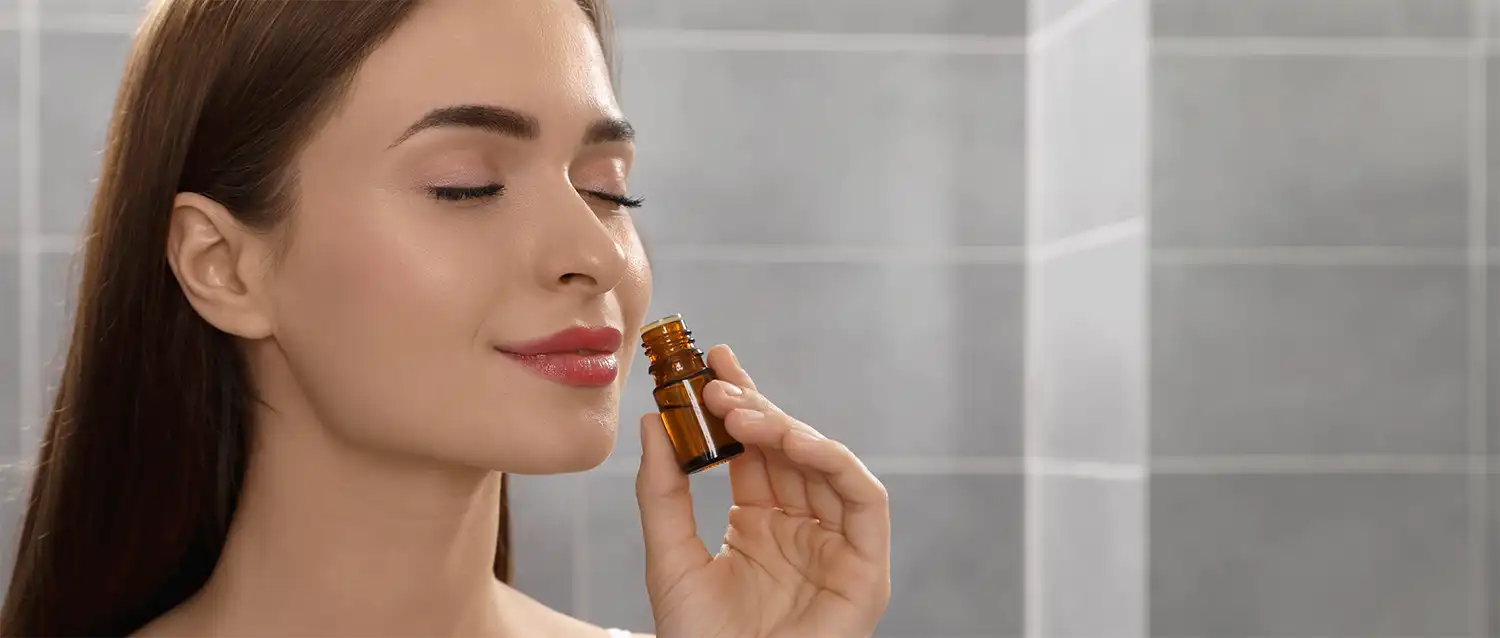 A woman smiling while inhaling a beautiful smelling essential oil